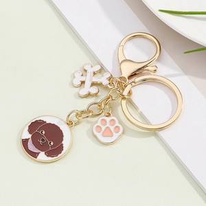 Detail of dog keychain with poodle tag, white bone charm, and pink paw on gold clasp