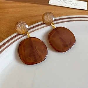 Detail of round coffee resin earrings on a white plate with a warm wooden background