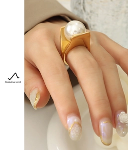 Close-up of chunky gold stainless steel ring with large white pearl on model's hand
