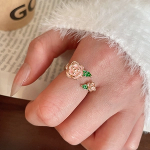 Gros plan d'une bague double rose avec feuilles vertes portée sur fond de papier rétro