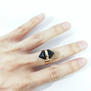 Detail of a minimalist gold ring featuring a hexagonal black crystal stone on a hand
