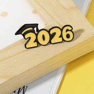 Macro shot of 2026 graduation cap enamel pin in black and yellow on wood frame