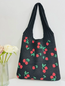 Detail of black knitted tote bag featuring red and green cherry patterns and integrated handle