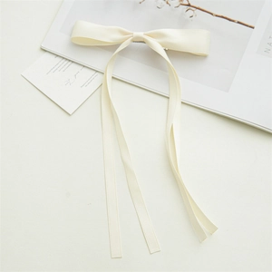 Detail showing elegant cream satin bow hair clip with long flowing ribbon streamers