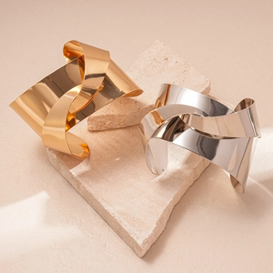Polished gold and silver geometric knotted cuff bracelets displayed on natural stone