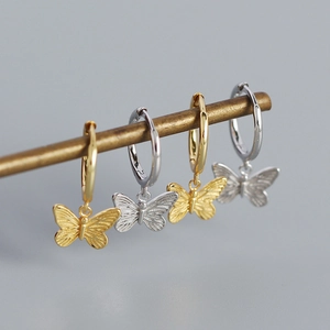 Detalle de pendientes de mariposa dorados y plateados en una barra de metal
