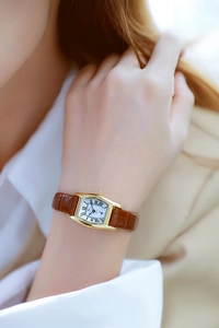 Close-up of rectangular gold watch with white Roman dial and brown leather strap