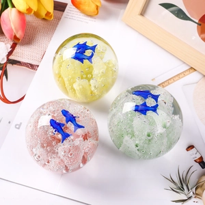 Detailed view of glass paperweights with blue fish designs and bubble art in three colors