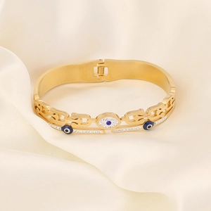 Nahaufnahme des goldenen Evil-Eye-Armreifs mit blauen Steinen auf Goldseide