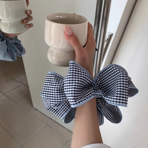Close-up of black and white gingham scrunchie with blue stitching in a lifestyle setting