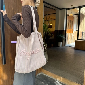 Detail of pink striped canvas tote bag with Bonjour embroidery shown on shoulder
