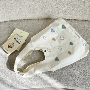 Close-up of heart embroidery and black snap button on white canvas tote bag