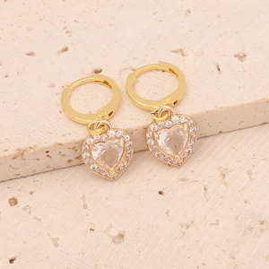 Close-up of gold-plated heart earrings with sparkling zircon stones on stone background