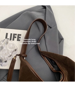 Detail of dark brown suede shoulder bag featuring a wide strap and minimalist leather tag