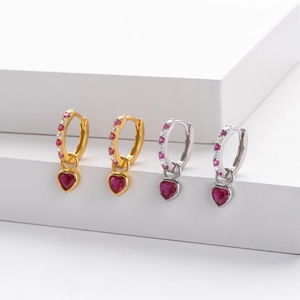 Detailed view of silver and gold heart earrings with ruby red crystals on white steps