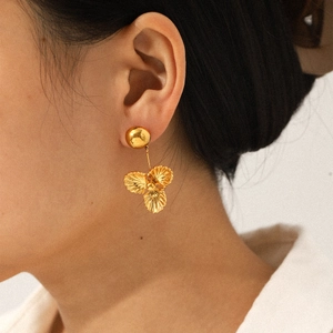 Gros plan d'un mannequin portant des boucles d'oreilles fleur en acier doré 18 carats