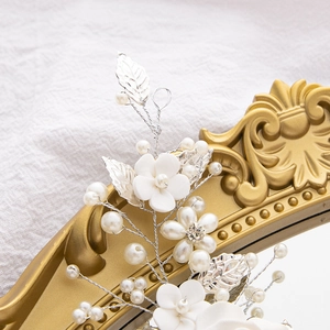 Detail of bridal headband with white ceramic flowers, pearls, and silver leaves on a mirror