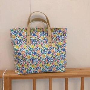 Close-up of floral canvas tote bag with brown leather handles and gold rivet details