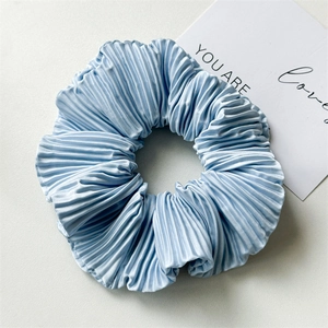 Detail of light blue pleated satin scrunchie with silky texture on a neutral background