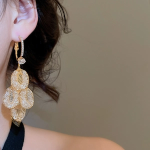 Close-up of golden leaf tassel earrings with zircon studs worn by a model in a side view
