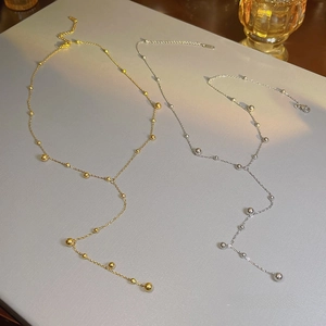 Close-up of gold and silver Y-shaped tassel necklaces with metallic beads on a textured surface