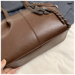 Close-up of brown PU leather tote bag detailing vertical stitching and woven rope charm