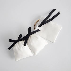 White velvet jewelry pouch with black ribbon bow and a gold bracelet inside