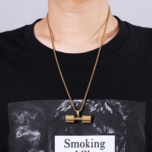 Close-up of golden dumbbell pendant necklace worn by a model against a plain background