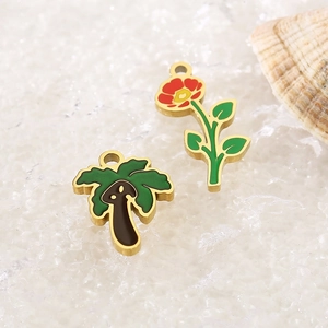 Close-up of golden enamel coconut tree and flower pendants on white sand and seashells