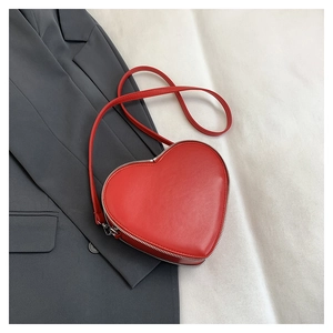 Detail of red heart-shaped crossbody bag with silver zipper on a gray blazer background