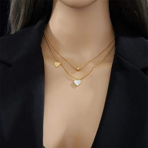 Double-layered gold necklace with heart and shell charms worn by a model on black suit