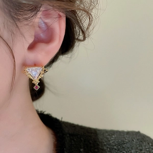 Détail de boucle d'oreille vintage dorée avec pierre triangulaire et cristal rouge