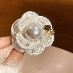 Macro detail of camellia brooch with woven fabric, central pearl, and golden number five