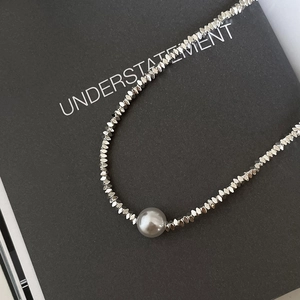 Macro detail of silver faceted beads and a single white pearl on a minimal necklace