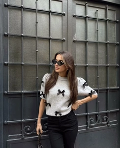Détail d'un pull en maille gris clair à manches courtes orné de petits nœuds noirs élégants