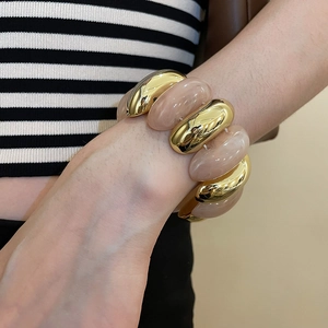 Detail of pink marble resin and gold oval link bracelet on wrist with striped shirt