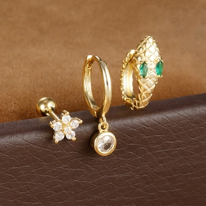 Golden S925 silver snake earring set with green cubic zirconia on leather surface
