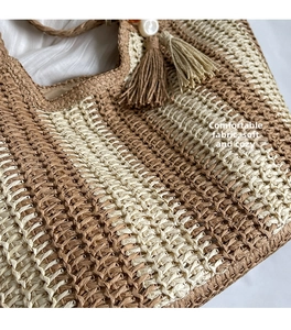 Detailed view of woven straw tote bag featuring brown stripes and decorative tassel
