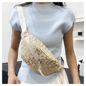 Detail of beige woven fanny pack with gold texture and adjustable strap worn by model