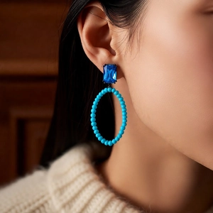 Close-up of vintage oval beaded earrings with blue gemstone on model showing retro design