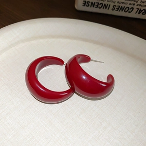 Detailed view of red glossy C-shaped hoop earrings on a light tray with soft lighting