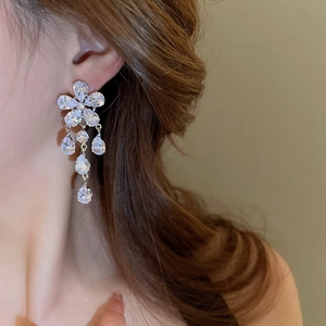 Detail of silver drop earrings with floral zircon tassels worn by a model in soft light