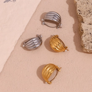 Detail of ribbed gold and silver steel earrings with white pearls on neutral stone back