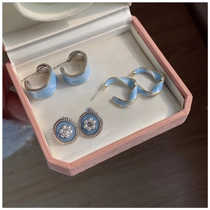 Close-up of blue enamel earrings and pearl studs displayed in a pink jewelry box