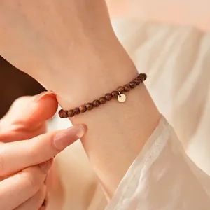 Minimalist dark wood beaded bracelet with a gold circular charm on a female wrist