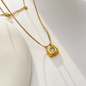 Detail of flower-shaped pendant with clear zircon and golden box chain on minimalist backdrop
