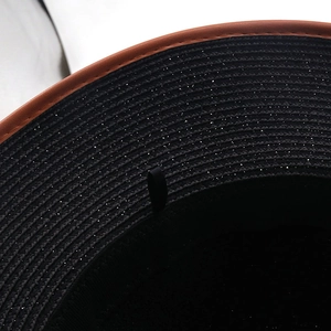 Macro view of woven black straw hat material with glitter and brown leather brim edging