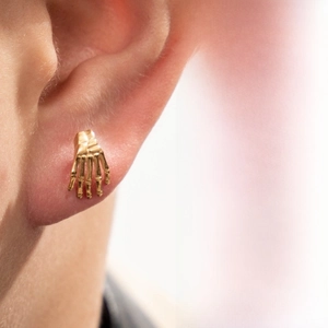 Detail view of a gold skeleton hand ear stud with intricate bone structure in punk style