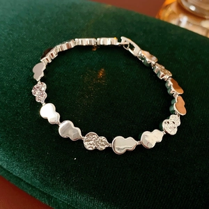 Macro detail of silver gourd link bracelet with hammered texture on green velvet background