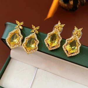 Detailed view of luxury gold teardrop earrings with crystal accents on a green velvet box